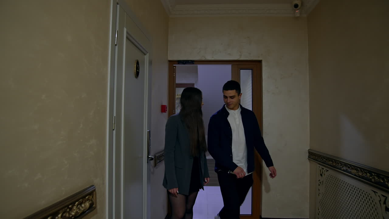 Young couple entering the hall. Girl taking a guy by the arm and they walk smiling to each other along the corridor.