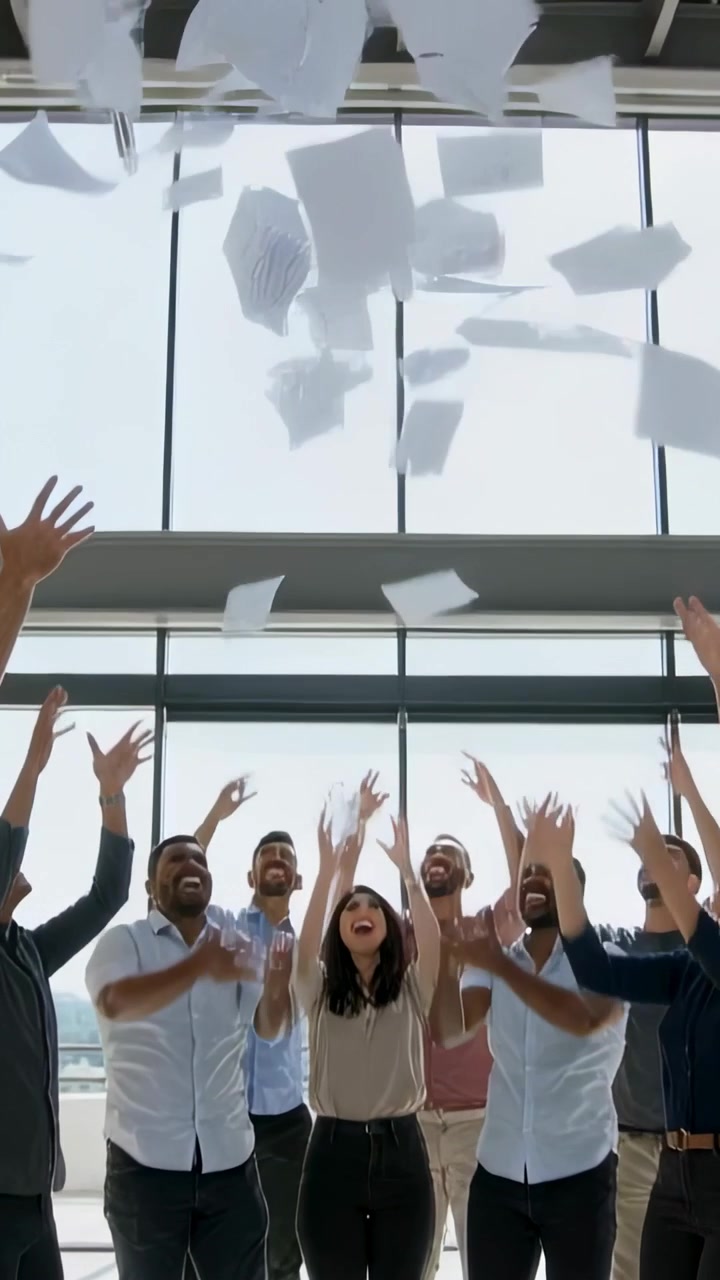 Vertical video: Throwing team tossing papers up at office windows after project, in office clothes