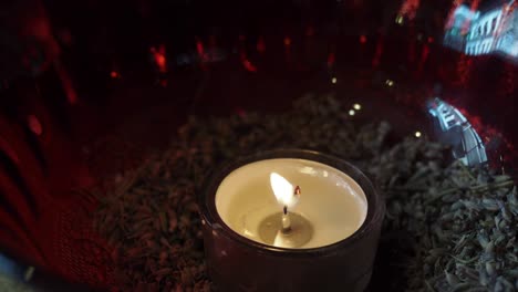 una sola vela ardiendo en un cuenco de vidrio rojo lleno de lavanda