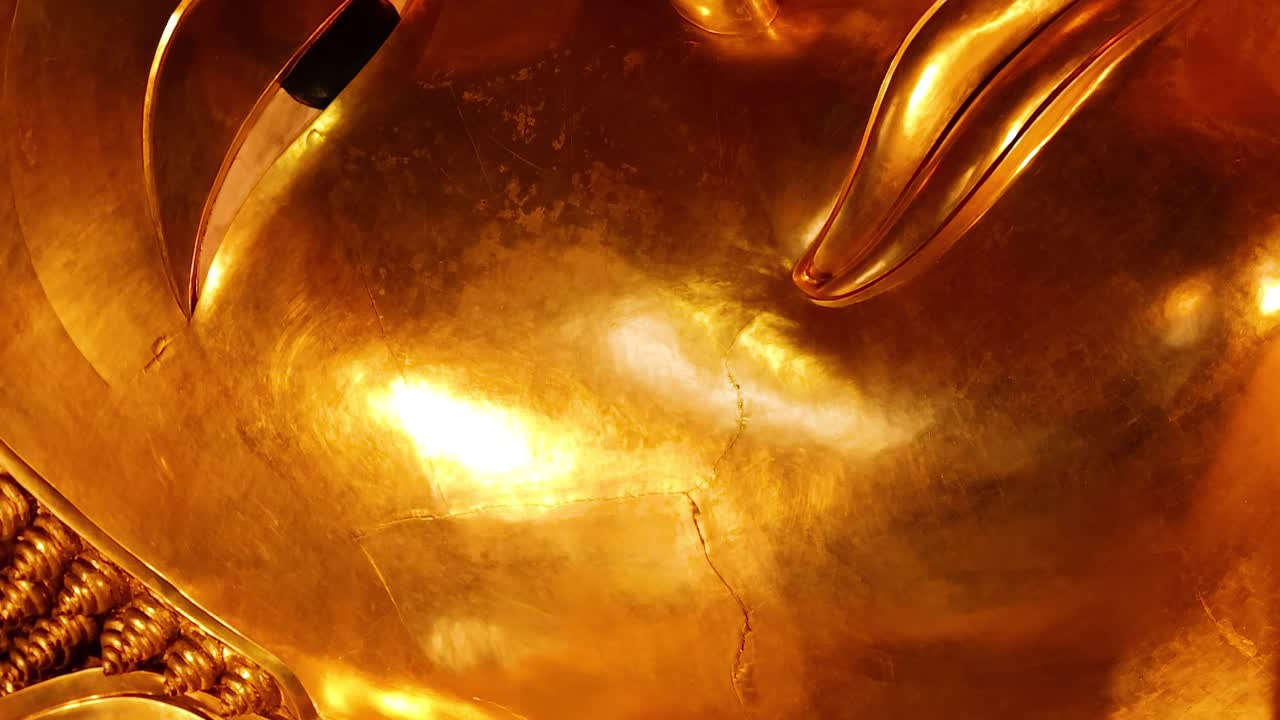 Close-up of a golden statue's face with intricate patterned background, highlighting serene expression and detailed craftsmanship.