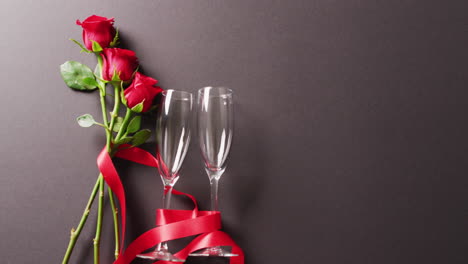 video of red rose flower stems and two champagne glasses on dark grey background with copy space