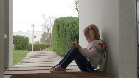 Little-girl-playing-on-the-phone-when-sitting-by-the-home-entrance