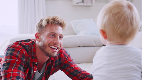 Young-dad-lying-on-floor-playing-with-toddler-son,-close-up