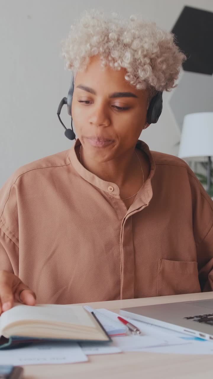 Young african american woman in headset sits at table with laptop in office