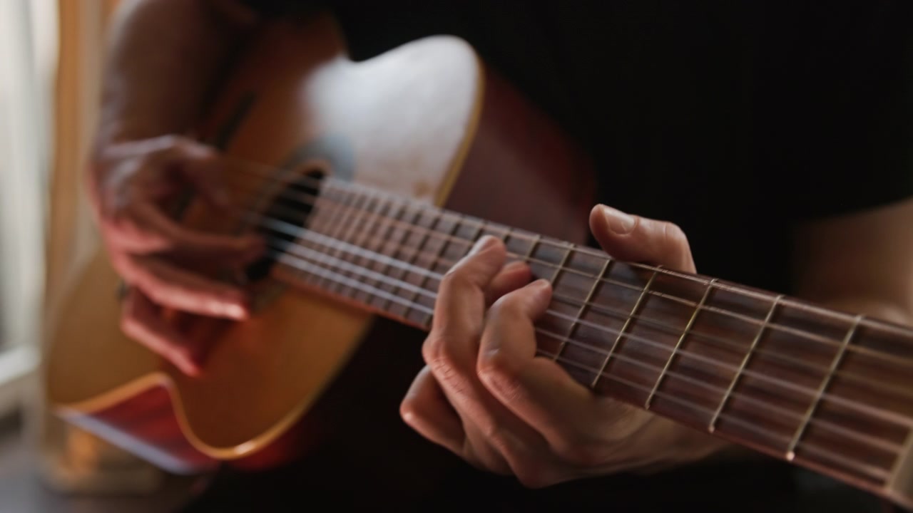 Primo piano di una persona che suona una chitarra classica acustica, eseguendo un assolo al rallentatore usando la tecnica fingerstyle. Il video presenta una bellissima illuminazione realistica e calda e un'ottima qualità estetica visiva.