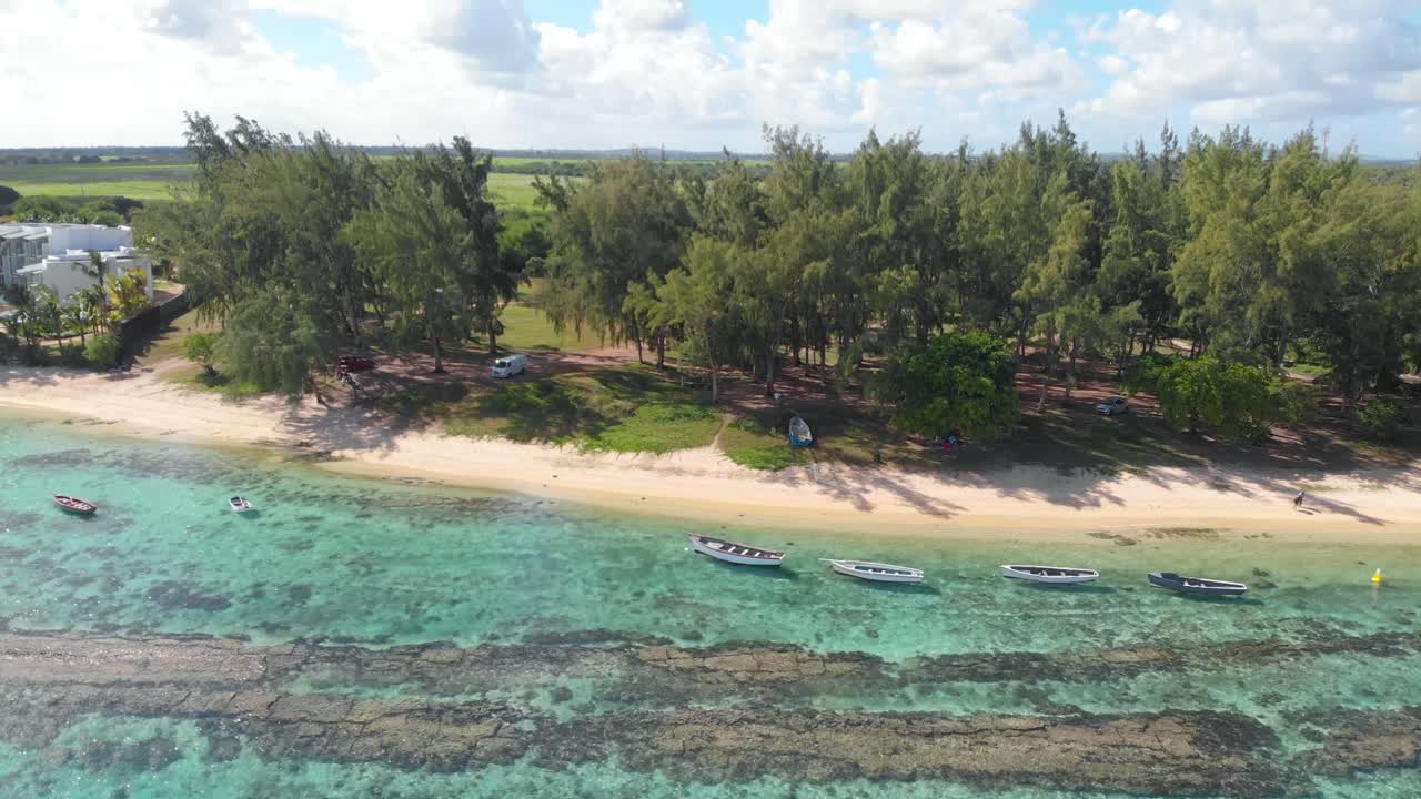 Inquadratura aerea 4K grandangolare di stabilimento di acqua cristallina che si avvicina alla spiaggia con barche a remi e palme a Balaclava, Mauritius.
