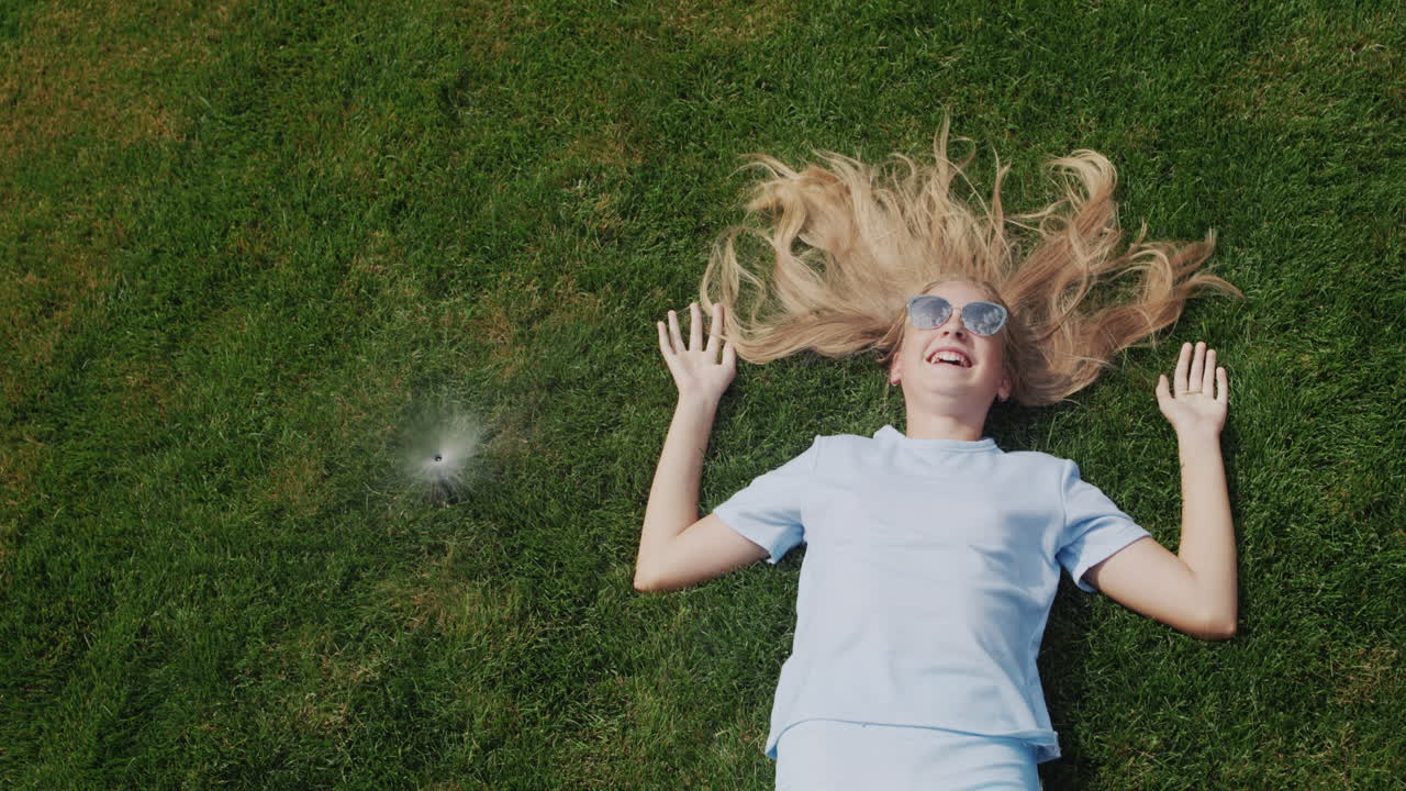 un niño con el pelo largo se acuesta en el césped bajo chorros de agua, escapa del calor intenso