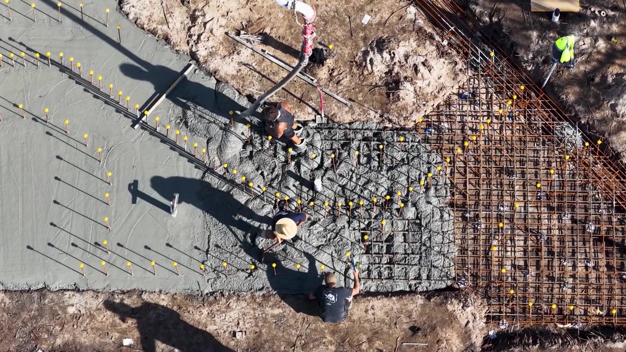Construction workers pour wet concrete over a steel rebar grid on a building site.