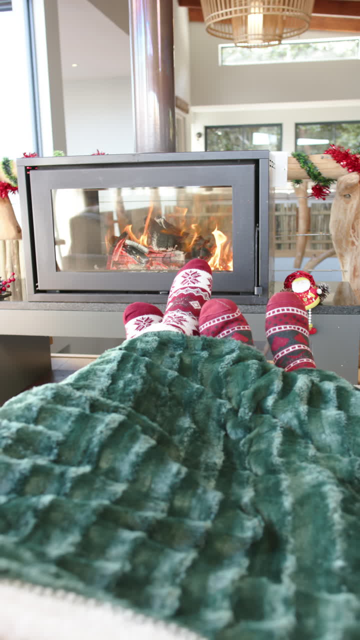 Vertical video of feet of diverse gay male couple on sofa by fireplace at home, slow motion