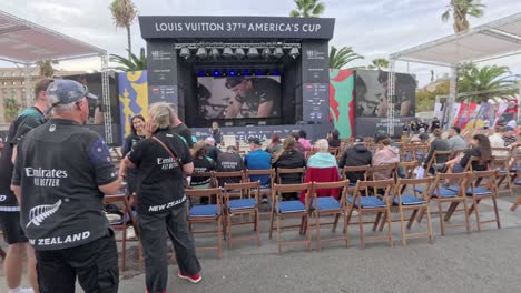 crowd outside watching the 37th america´s cup on a giant screen. drinks