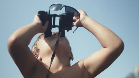 young boy using binoculars and look up into the bright blue sky on a sunny summer day