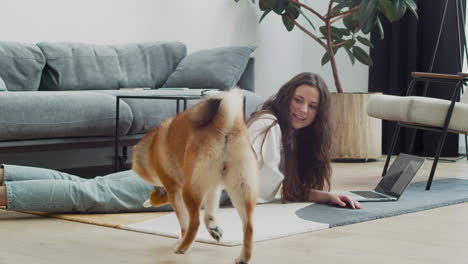 linda chica juega con su perro mientras trabaja en su computadora portátil en casa