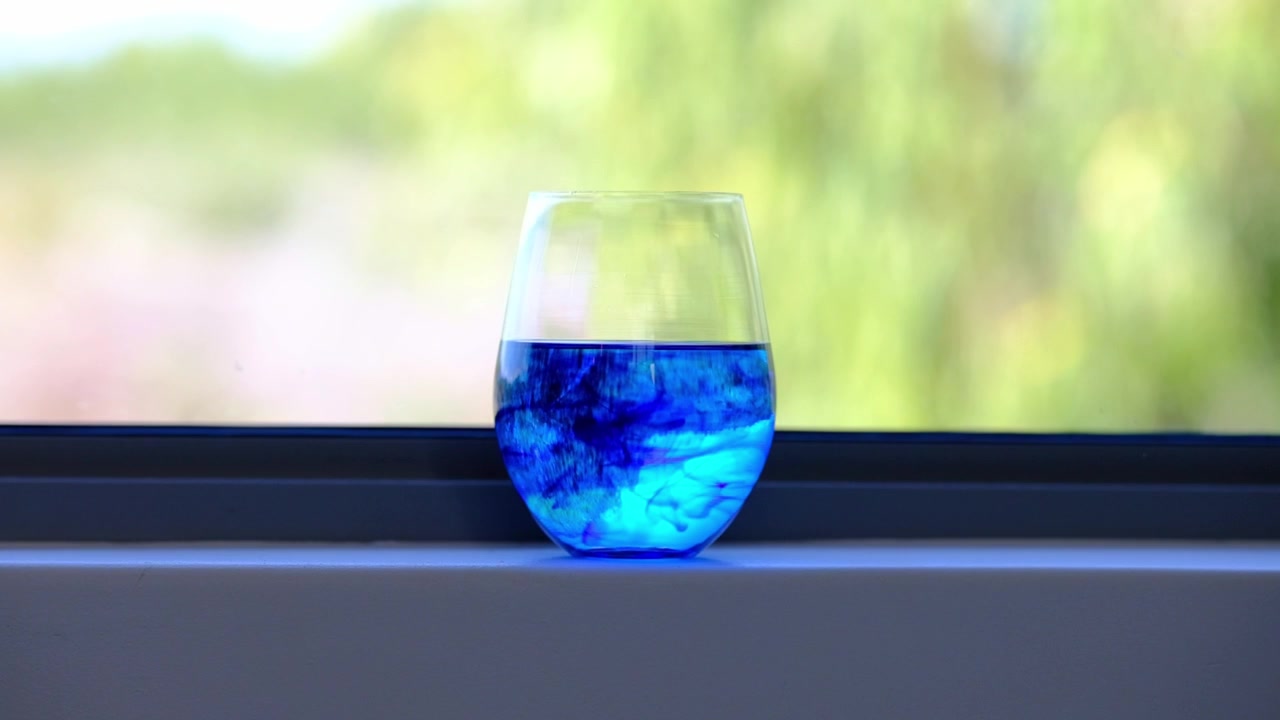 Un bicchiere di Blu di Metilene su un davanzale che si diluisce lentamente nell'acqua.