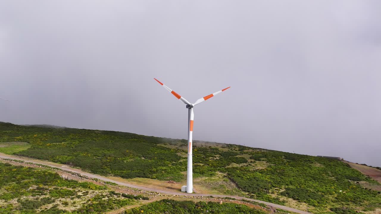 Turbine eoliche che girano su un crinale verde con una nebbia montana inquietante sullo sfondo.