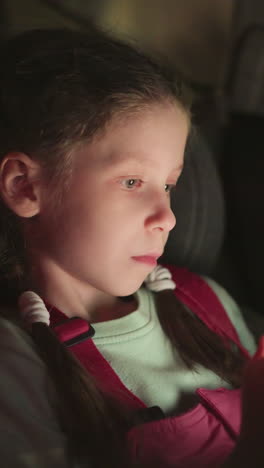 una vista de cerca de un niño que opera un teléfono celular en el coche con un rostro de mal humor, el niño está centrado en la pantalla, con un mono rosa y una camisa verde claro