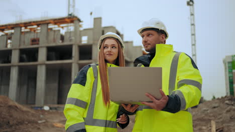 two civil engineers are discussing project and progress of construction of modern building outdoors man and woman