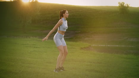 an active young woman in a park at sunset stands on one leg and jumps. lunges on each leg and jumps in the park in the summer