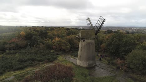 Traditional-wooden-stone-flour-mill-windmill-preserved-in-Autumn-woodland-aerial-view-countryside-slow-right-orbit