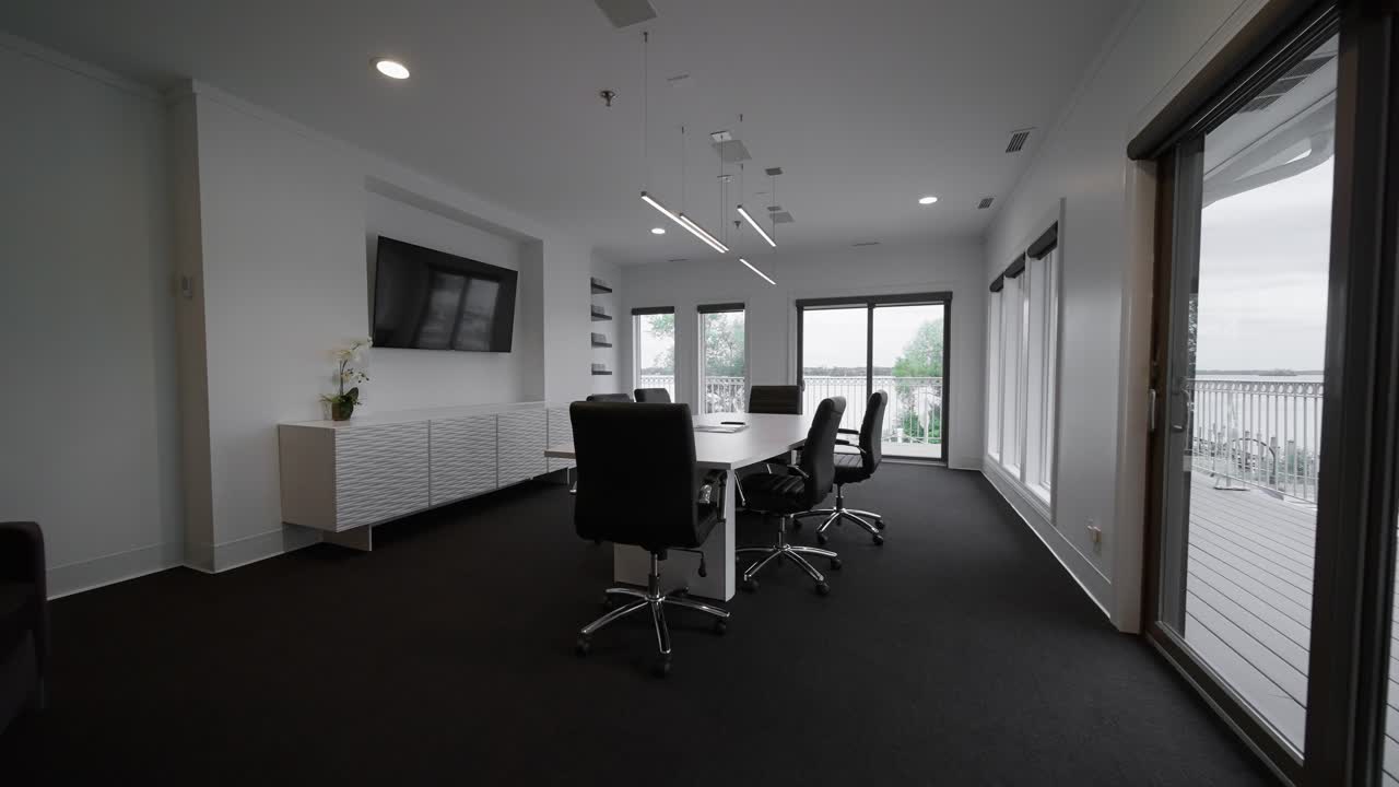 Plano de acercamiento amplio de una sala de conferencias con una mesa blanca, sillas negras y luz natural