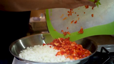 tirando pimientos rojos picados en una sartén con cebollas frescas como parte de una receta casera - cámara lenta
