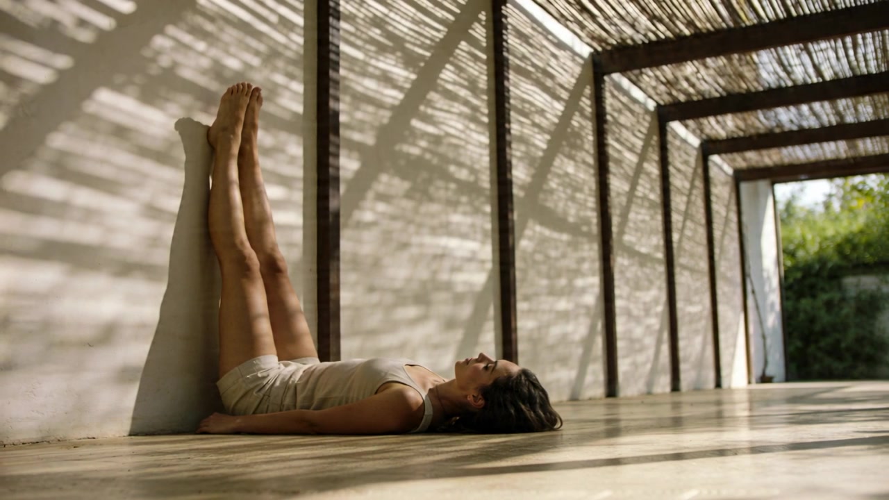 Resting woman shifting on terrace while sunlight moving, pergola shadows, in light shorts and top