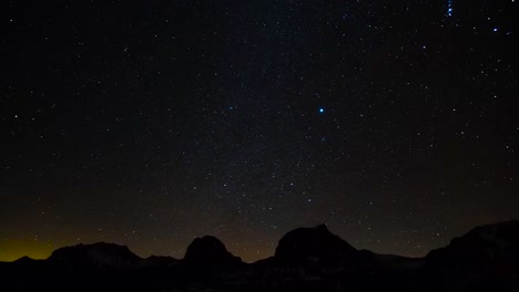 time lapse or timelapse footage of a starry night or evening sky with bright stars. mountain silhouettes are visible in the background and a small orange and yellow glare behind the mountains in 4k.