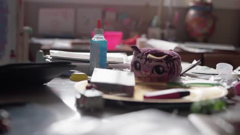 a stuffed cat animal is on a table with glue, papers and various arts and craft items.