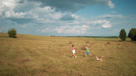 distant view of cheerful children running through golden field with small dog on leash, sister in pink top leads, while brother in green follows, sunlit countryside setting with scattered hay bales