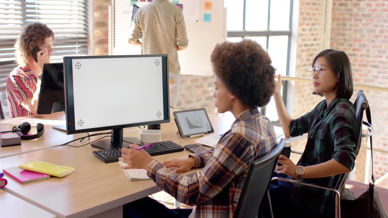 Two happy diverse businesswomen using computer in casual office, copy space on screen, slow motion