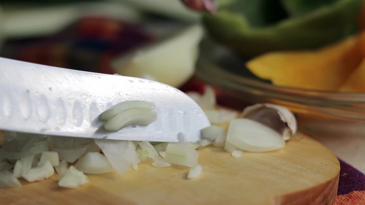 Extreme close up shot of a woman's hand using a knife to chop onion on a cutting board into small pieces - Slowmotion panning shot
