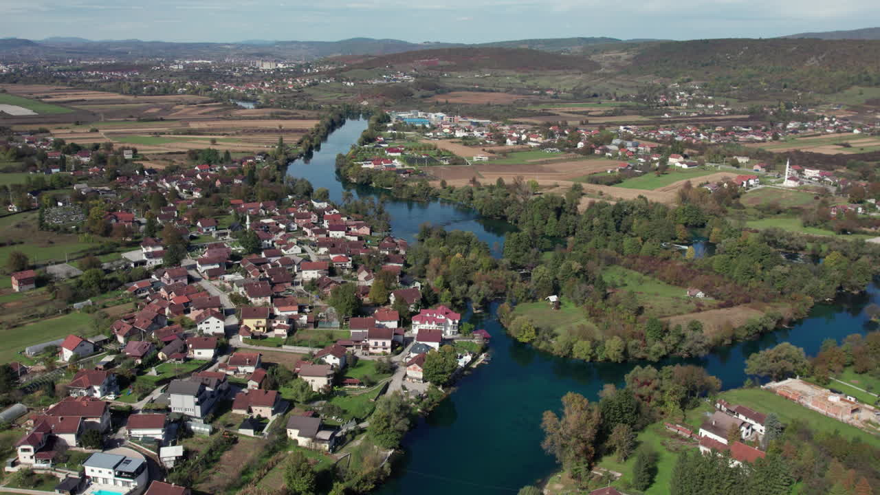 Aerial drone view of the winding Una River surrounded by small villages, fields, and green landscapes near Bihać in Bosnia and Herzegovina. A scenic natural view of the Balkan countryside in autumn