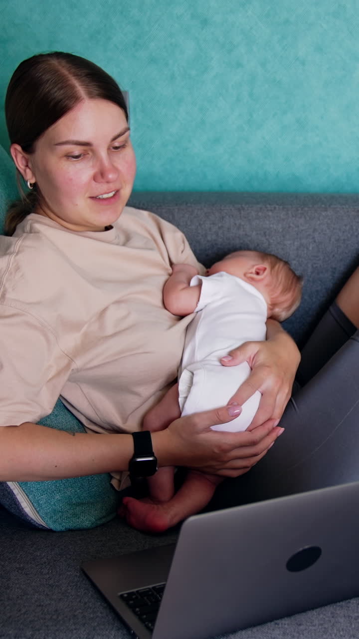 Caucasian mother combining work and childcare. Woman with child in arms works at laptop. Vertical video