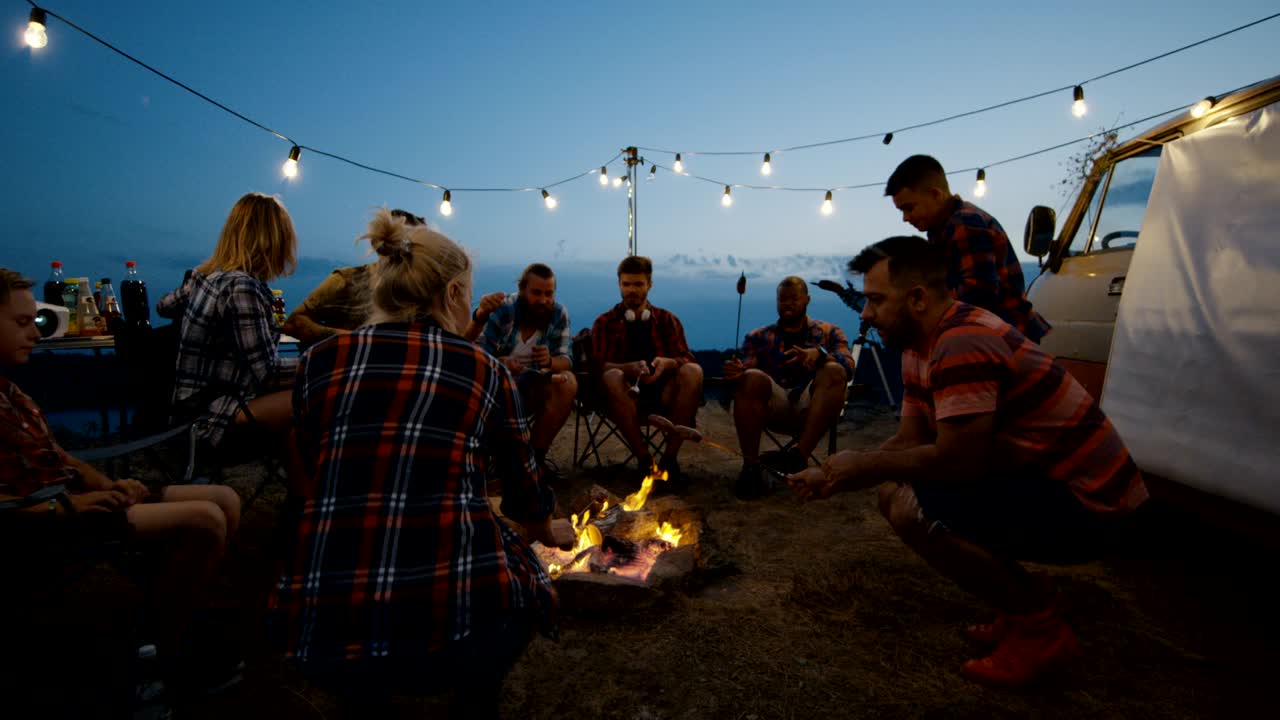 친구 들 이 황혼 에 캠프 불 에 소시지 를 고 있다