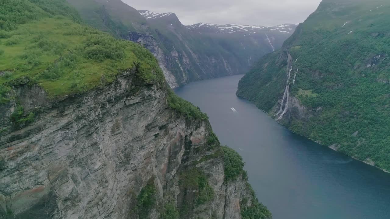 slomo aéreo do fiorde de geiranger, noruega, voando em direção a uma montanha com um barco em movimento ao fundo, passando pelas sete irmãs