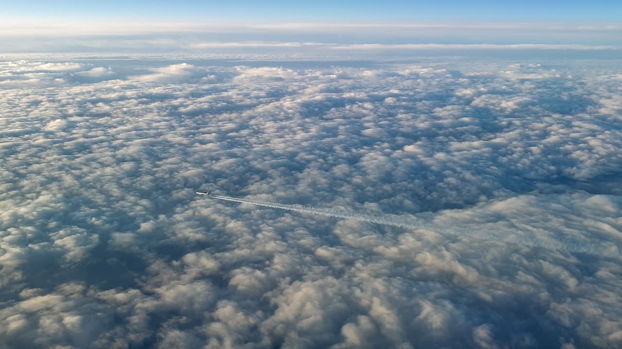 Incredible view from the cockpit of an airplane flying high above the clouds leaving a long white condensation vapour air trail in the blue sky
