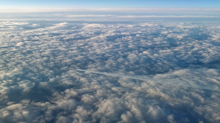 Utrolig udsigt fra cockpittet på et fly, der flyver højt over skyerne og efterlader et langt hvidt kondensationsspor på den blå himmel