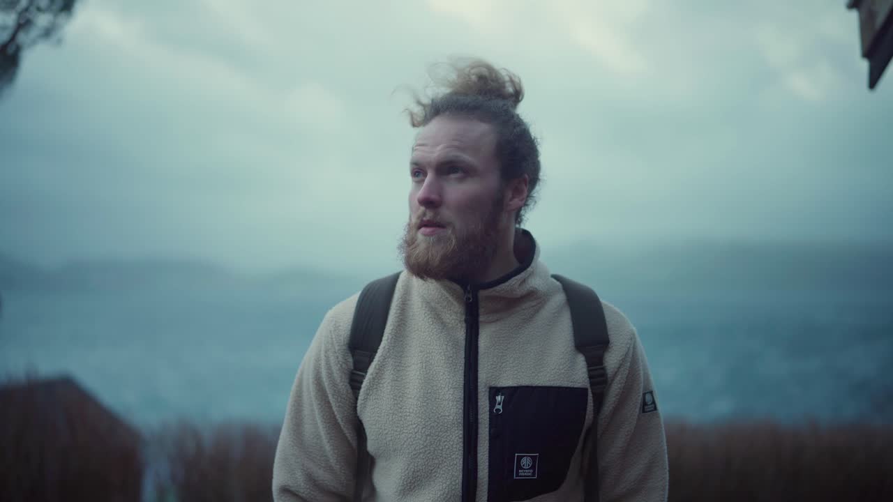 retrato de un europeo barbudo con el pelo largo parado y mirando a la cámara en un día frío y ventoso