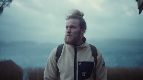 Portrait-Of-A-Bearded-European-Man-With-Long-Hair-Standing-And-Looking-At-Camera-On-Cold-Windy-Day