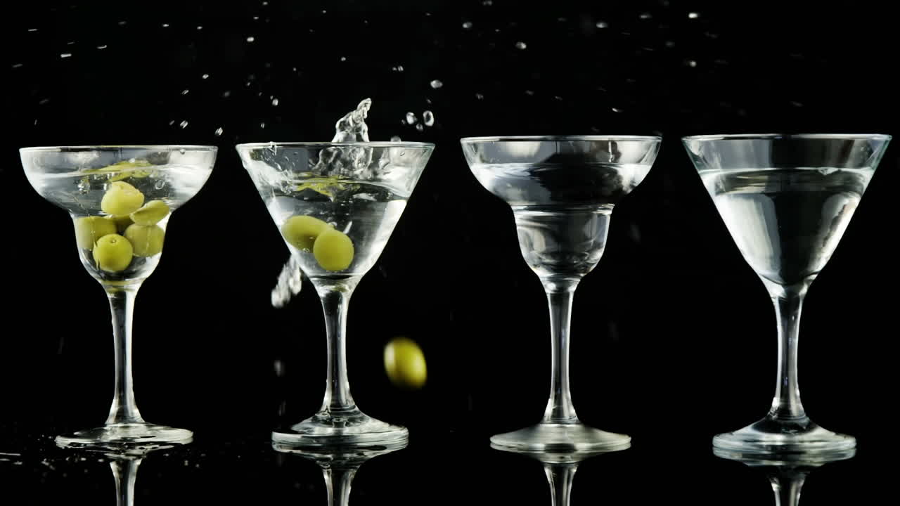 papel gris quemando sobre las aceitunas que caen en copas de cóctel contra un fondo negro