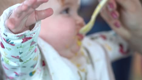 un niño hambriento está siendo alimentado con cuchara por la mano de una madre, toma de cerca desde un lado, dentro y fuera de foco - cámara lenta