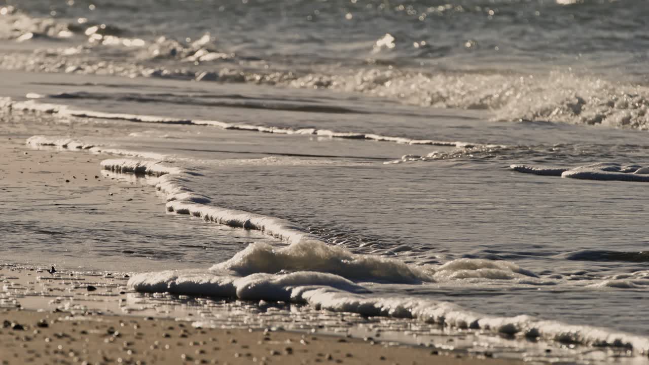 A gentle wave rolls onto the shore near the Oosterschelde barrier, Zeeland, Netherlands, super slow motion