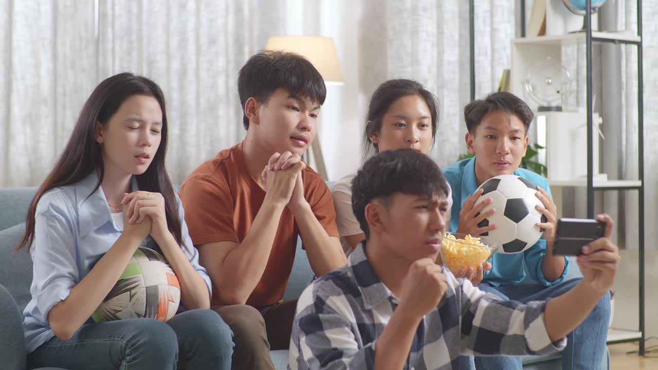 아시아 십대 들 이 집 에서 스마트폰 으로 축구 경기 를 시청 하고 응원 하고 있다