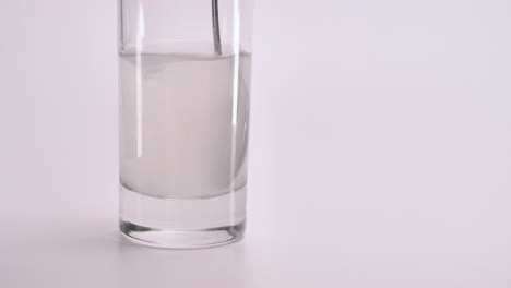 Mixing-powder-with-a-spoon-in-a-glass-of-clean-water-on-a-white-background