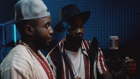 portrait shot of the two young happy stylish guys singers or rappers standing in the sound studio at the mic and smiling cheerfully to the camera