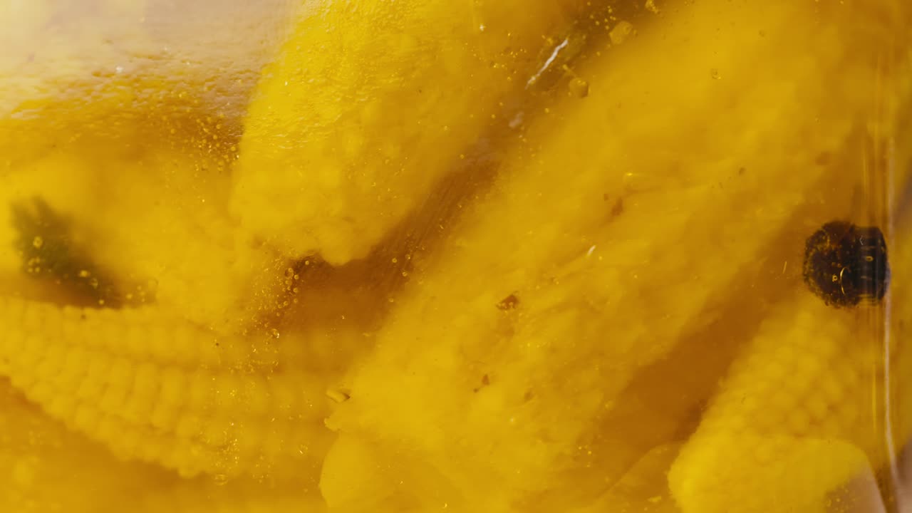 Close-up of fermented yellow mini corn with black pepper in can. Preservation of vegetables in glass jars. Fermentation preserved mini corns with spices.