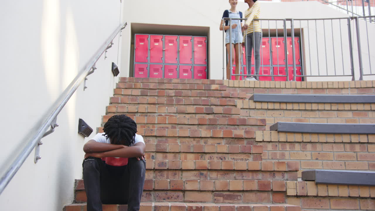 Sitting on stairs, student feeling sad while classmates talking in school, copy space