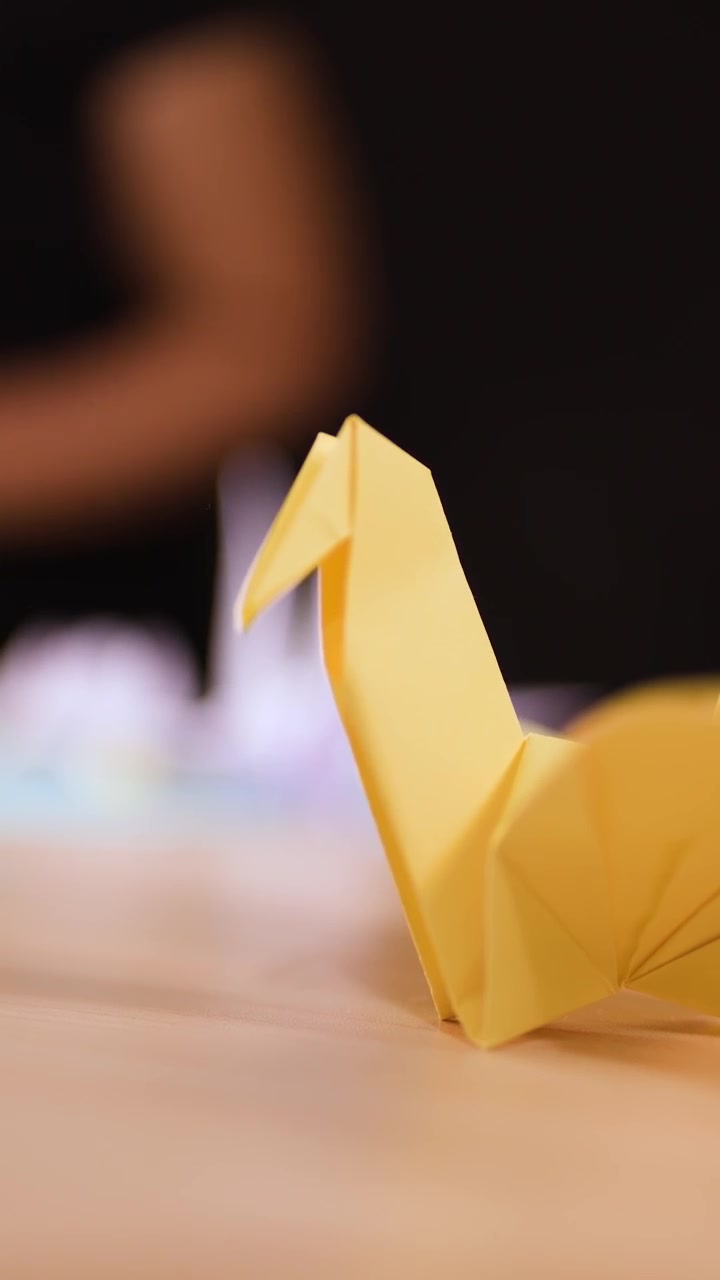A static close-up shot of a completed yellow paper crane resting on a wooden surface