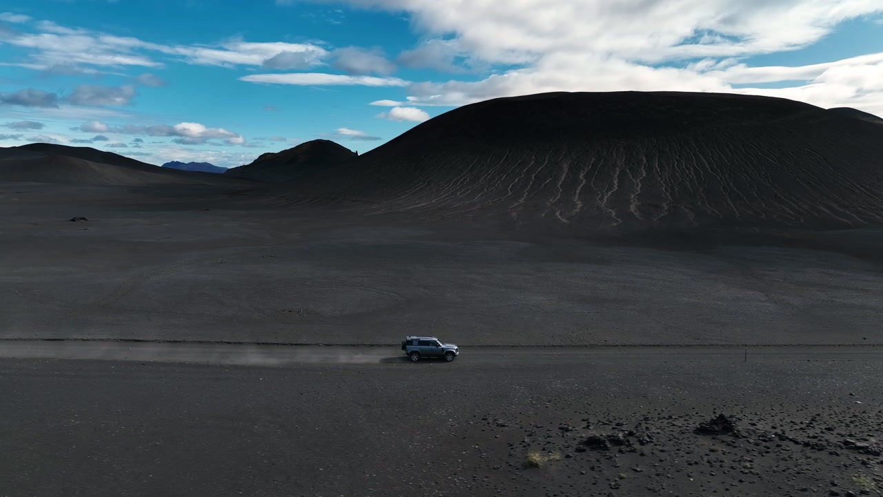 Off-road vehicle driving through volcanic sand and rugged hills in Iceland, showcasing wild and dramatic scenery in road trip.
