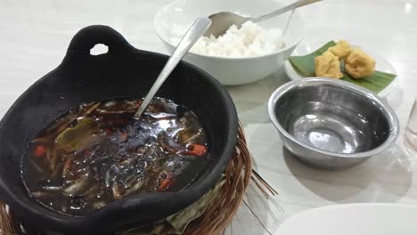 squid cooked mandar typical of west sulawesi province. squid in black ink sauce with spicy seasoning. indonesian home cooking menu with chili, ginger, and lime leaf seasoning served in a large pot.