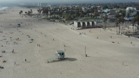 AERIAL:-Circling-around-Venice-Beach-skatepark-and-boardwalk-with-palm-trees-and-bike-lane,-Sunny,-Los-Angeles-California